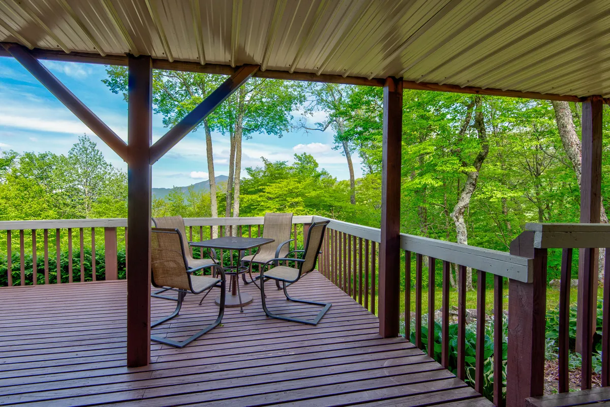 A tranquil outdoor area featuring comfortable seating under the shade of mature green trees, with panoramic mountain vistas in the background. The relaxed setting encourages socializing or simply enjoying the peacefulness with pets by your side.