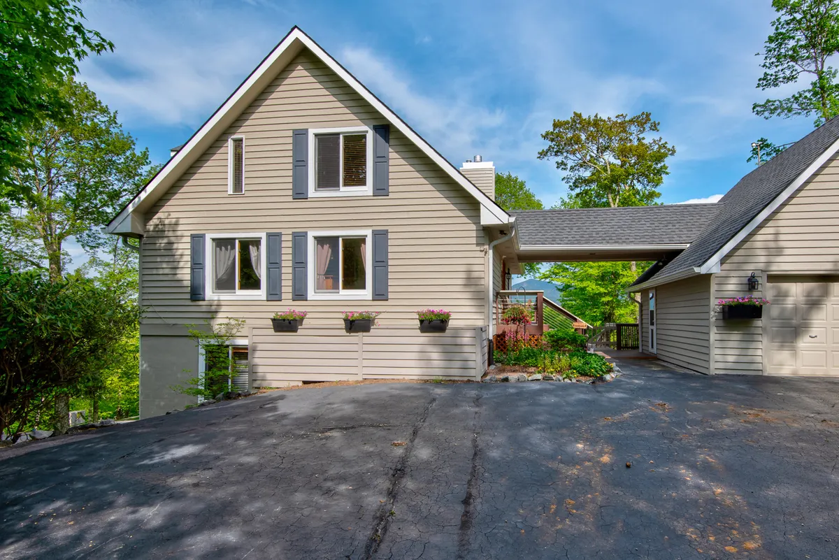 This image showcases the main entrance of the home, with a front door framed by window shutters and vibrant flower boxes. The driveway suggests easy access, while the porch provides a sense of calm arrival, ideal for a luxury mountain retreat.