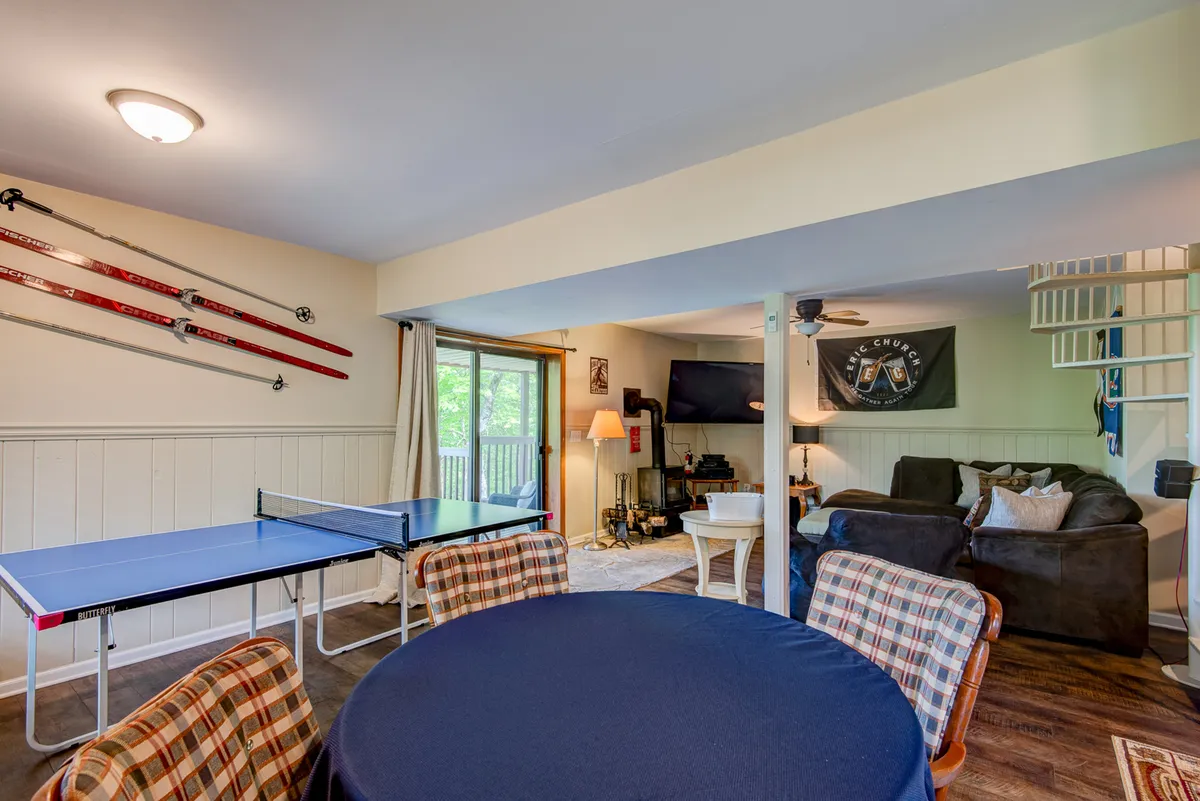 This image shows a lively game room featuring a ping pong table prominently in the foreground, a comfortable seating area, a television mounted on the wall, and decorative wall art. The ambiance is playful and relaxed, inviting guests to engage in friendly competitions or watch TV together.
