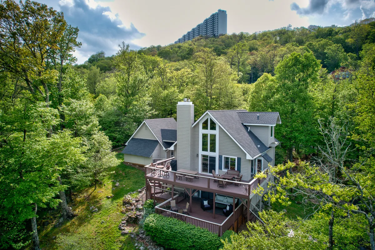 This exterior shot features the house with its deck surrounded by trees, suggesting easy access to nature and outdoor activities. The scene hints at the property's proximity to trails and scenic areas, aligning perfectly with the adventure-driven narrative of the section.