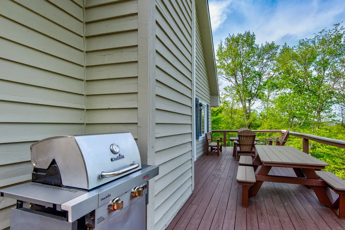 A barbecue grill and outdoor dining table sit on the deck, surrounded by trees and greenery. The space is clearly set up for social gatherings, with plenty of seating for group meals or evening cocktails under the stars.