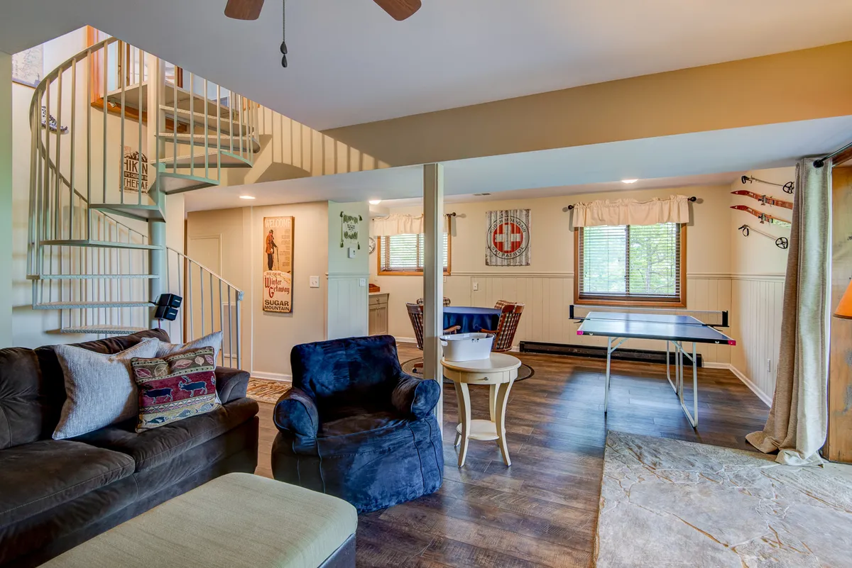 This interior photo captures another angle of the game room, showcasing the spiral staircase, a blue armchair for relaxing, the ping pong table, and a dining area. The scene is casual and welcoming, ideal for group activities or quiet moments alike.
