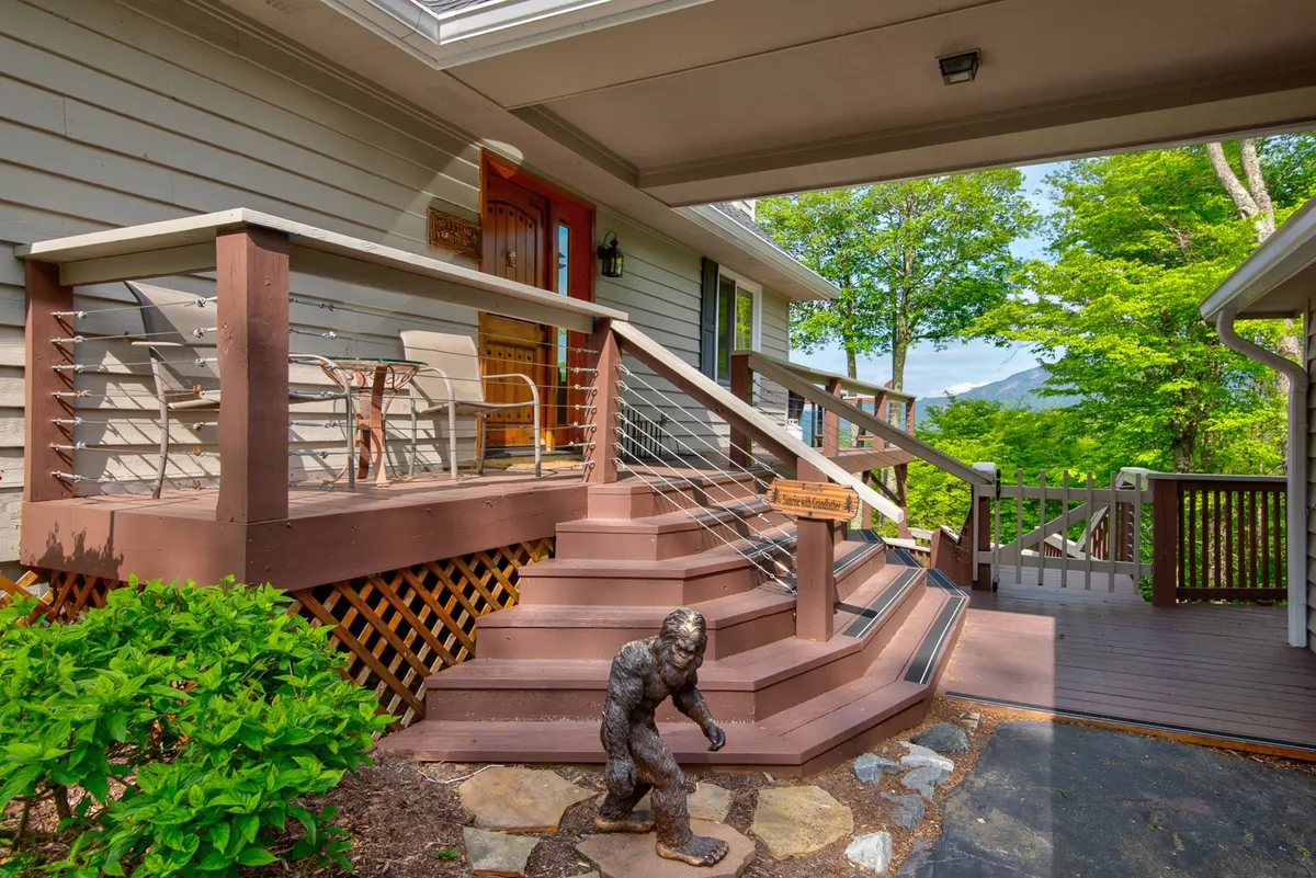 A welcoming exterior view featuring wooden stairs leading up to the front door, an outdoor seating area, and a playful bigfoot statue. The porch is ready for gathering and enjoying the sights and sounds of the outdoors with easy access—a fun, approachable first impression for guests with pets.