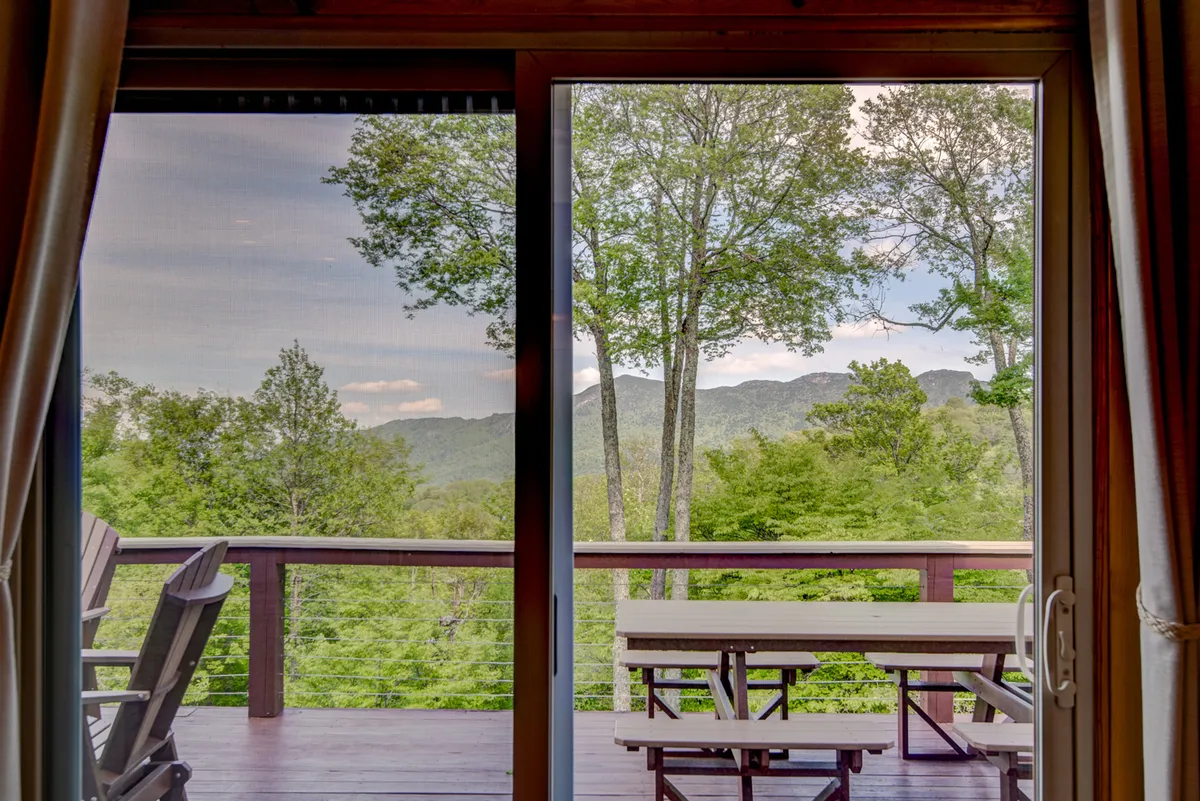 A spacious deck furnished with a picnic table and chairs, overlooking sweeping mountain views framed by mature trees. The setting is tranquil and designed for outdoor relaxation or dining after a day of adventures.