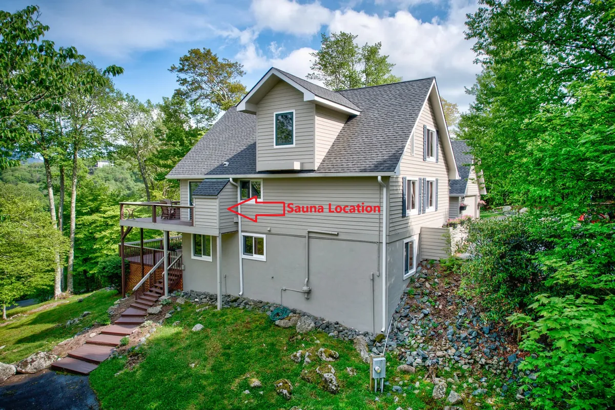 The exterior of the home is displayed, with the deck clearly visible alongside surrounding greenery and the location of the sauna. The scene conveys serenity and the seamless blend of indoor comforts with outdoor wellness amenities.